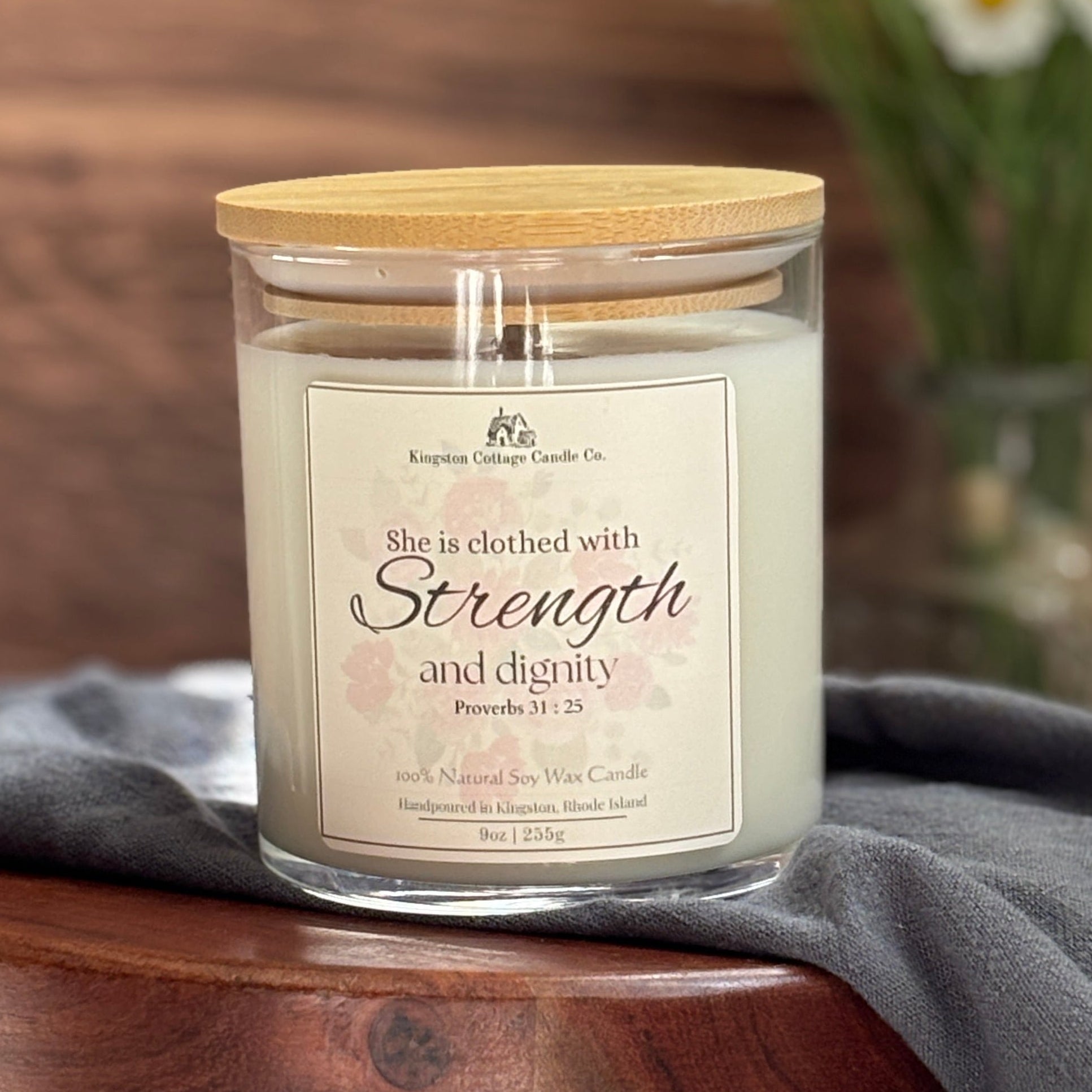 Candle with 'Strength and Dignity' message on a wooden stand with flowers in the background