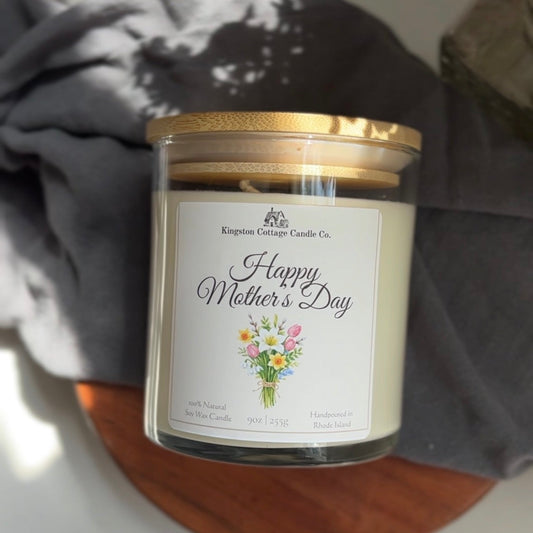 Candle in a glass jar with a 'Happy Mother's Day' label on a wooden surface.