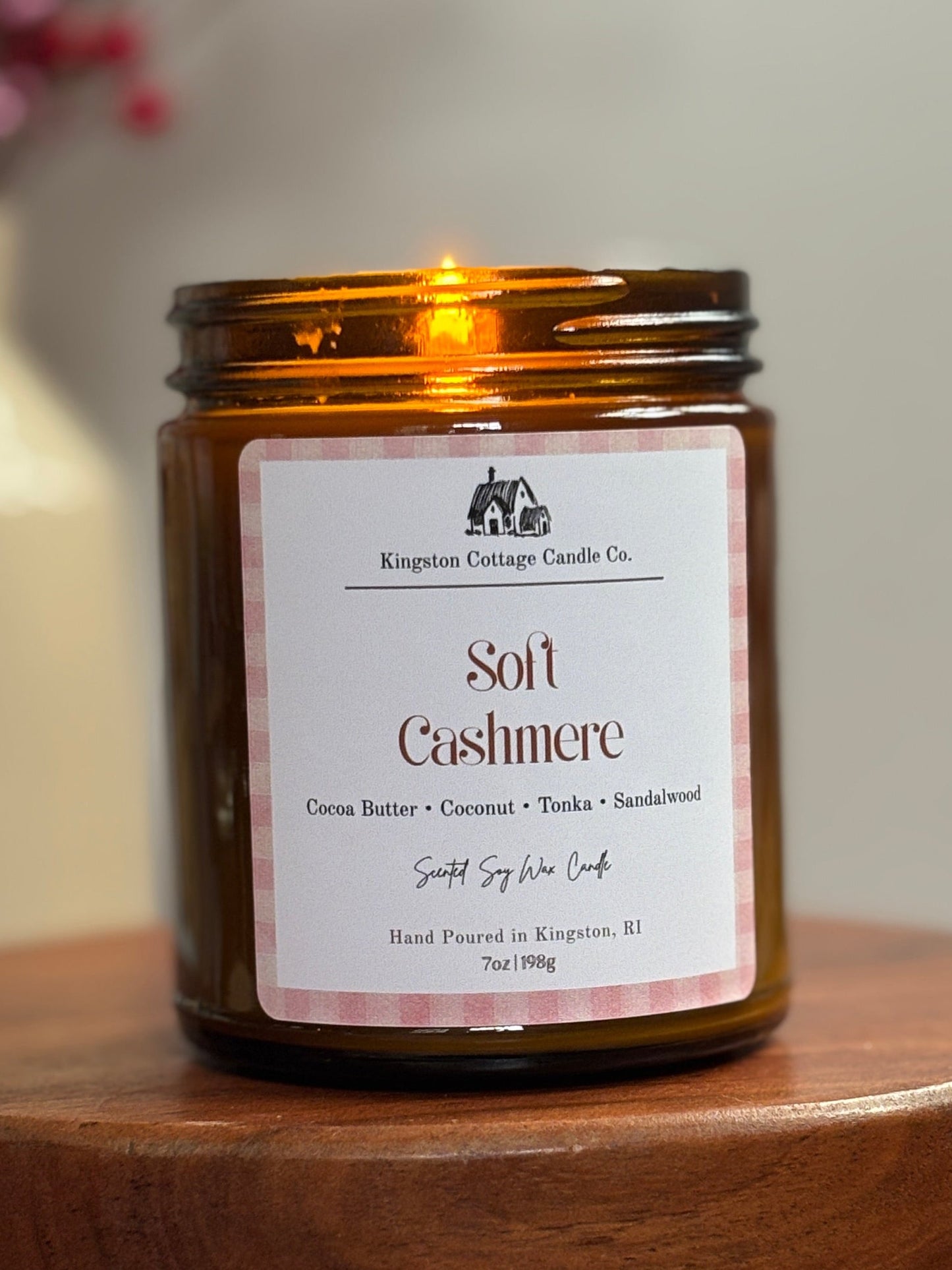 Candle jar labeled 'Soft Cashmere' on a wooden stand with a blurred background