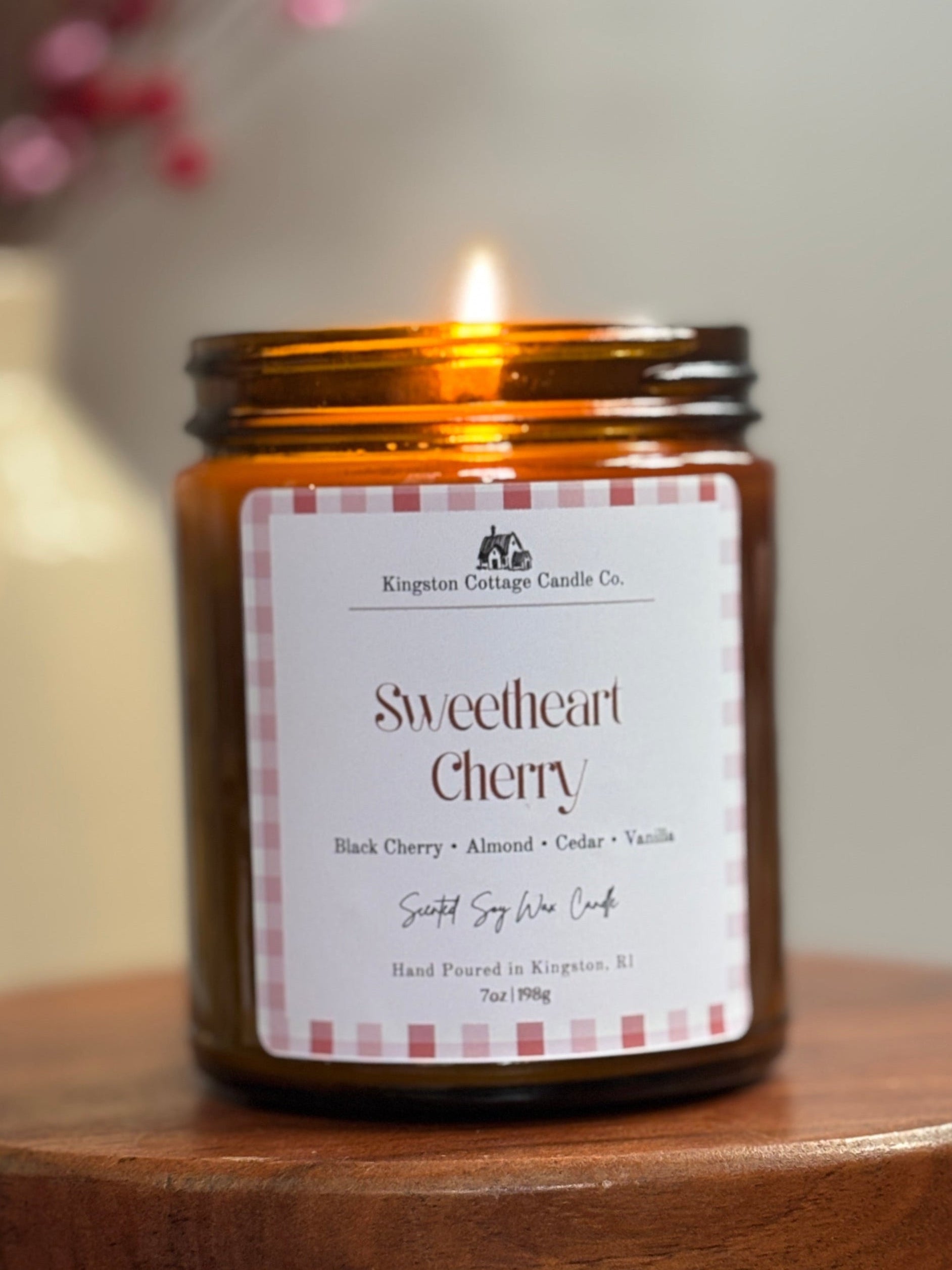 Candle labeled 'Sweetheart Cherry' on a wooden coaster with a blurred background